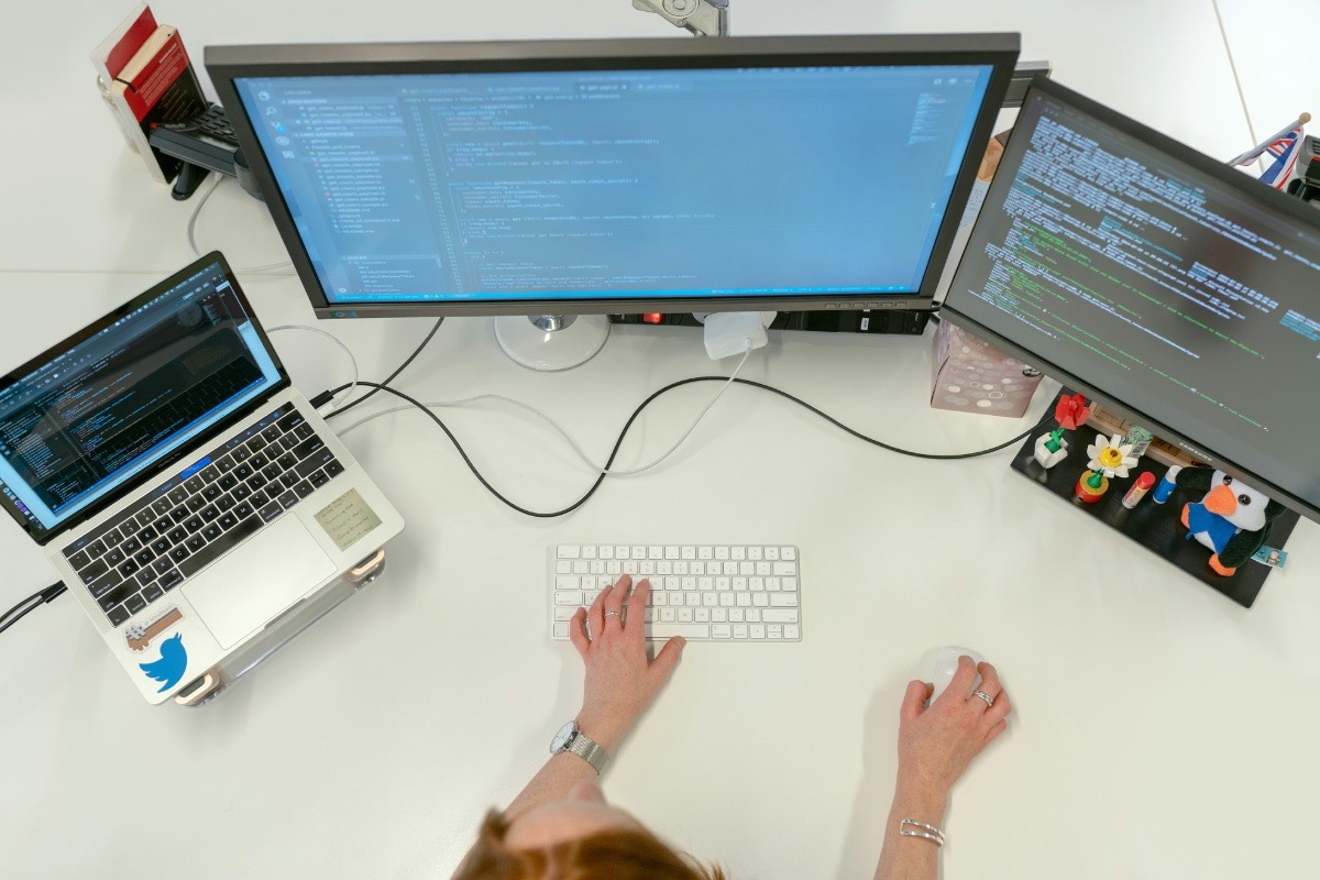 Overhead view of a software developer working across a laptop and two monitors showing application code