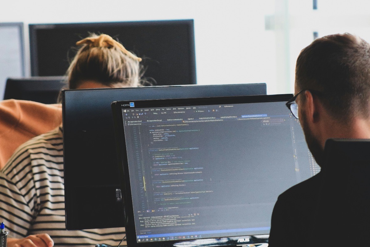 Two developers reviewing application code on a monitor in a shared office